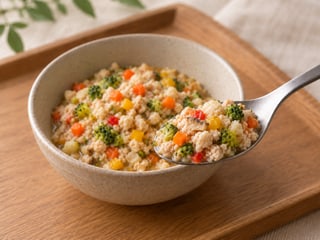 木のお盆に置いた器とスプーンに盛り付けた、鶏ももミンチと野菜のごはん